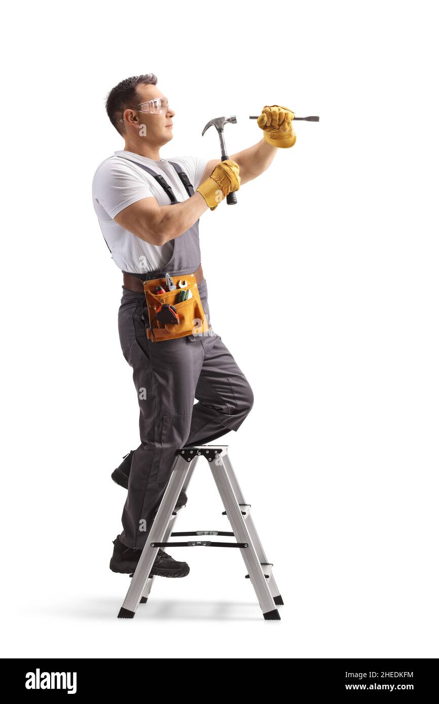 Plan en longueur d'un réparateur en uniforme debout sur une échelle et travaillant avec un marteau isolé sur fond blanc Banque D'Images Plan en longueur d'un réparateur en uniforme debout sur une échelle et travaillant avec un marteau isolé sur fond blanc Banque D'Images