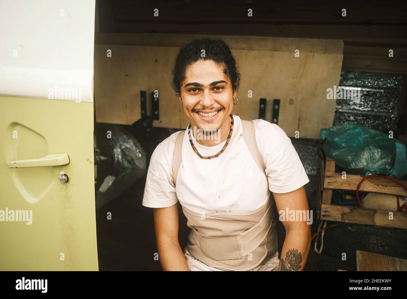 Un homme latino-américain positif dans des vêtements décontractés regardant l'appareil photo avec le sourire tout en étant assis dans une remorque moderne pendant un voyage en voiture Banque D'Images