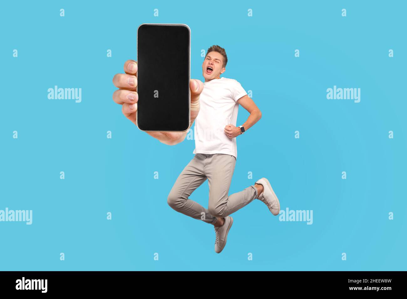 Homme heureux volant et sautant dans l'air et montrant grand écran mobile vide pour l'espace de copie et la zone publicitaire. Studio d'intérieur tourné isolé sur fond bleu Banque D'Images
