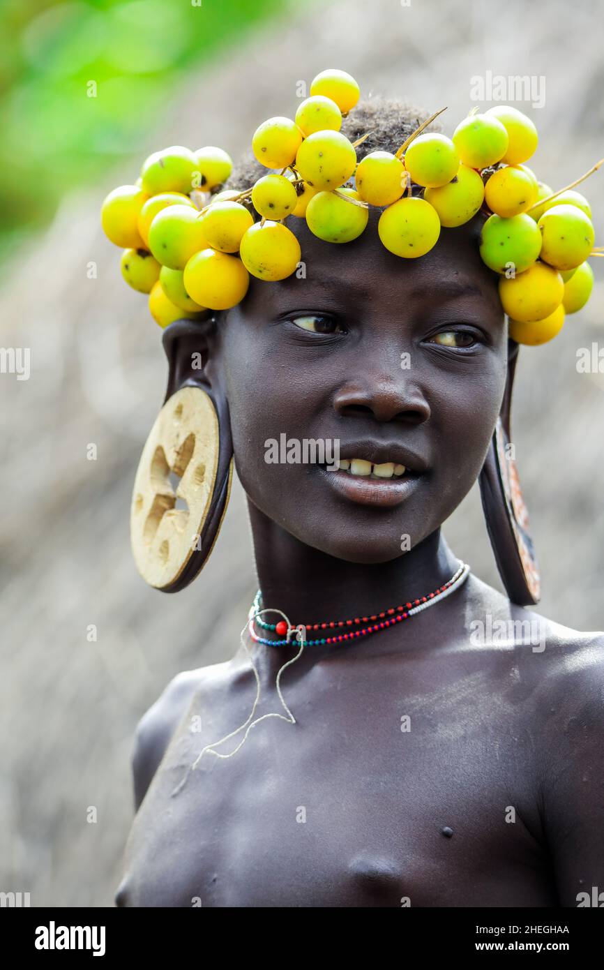 Omo River Valley, Éthiopie - 29 novembre 2020 : portrait d'un adolescent africain avec de grandes boucles d'oreilles traditionnelles en bois et une couronne de fleurs jaunes sèches Banque D'Images