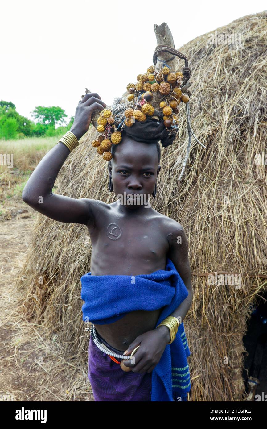 Omo River Valley, Ethiopie - 29 novembre 2020: Portrait d'un adolescent africain avec des boucles d'oreilles traditionnelles en bois et des cornes brisées avec des fleurs jaunes sèches Banque D'Images