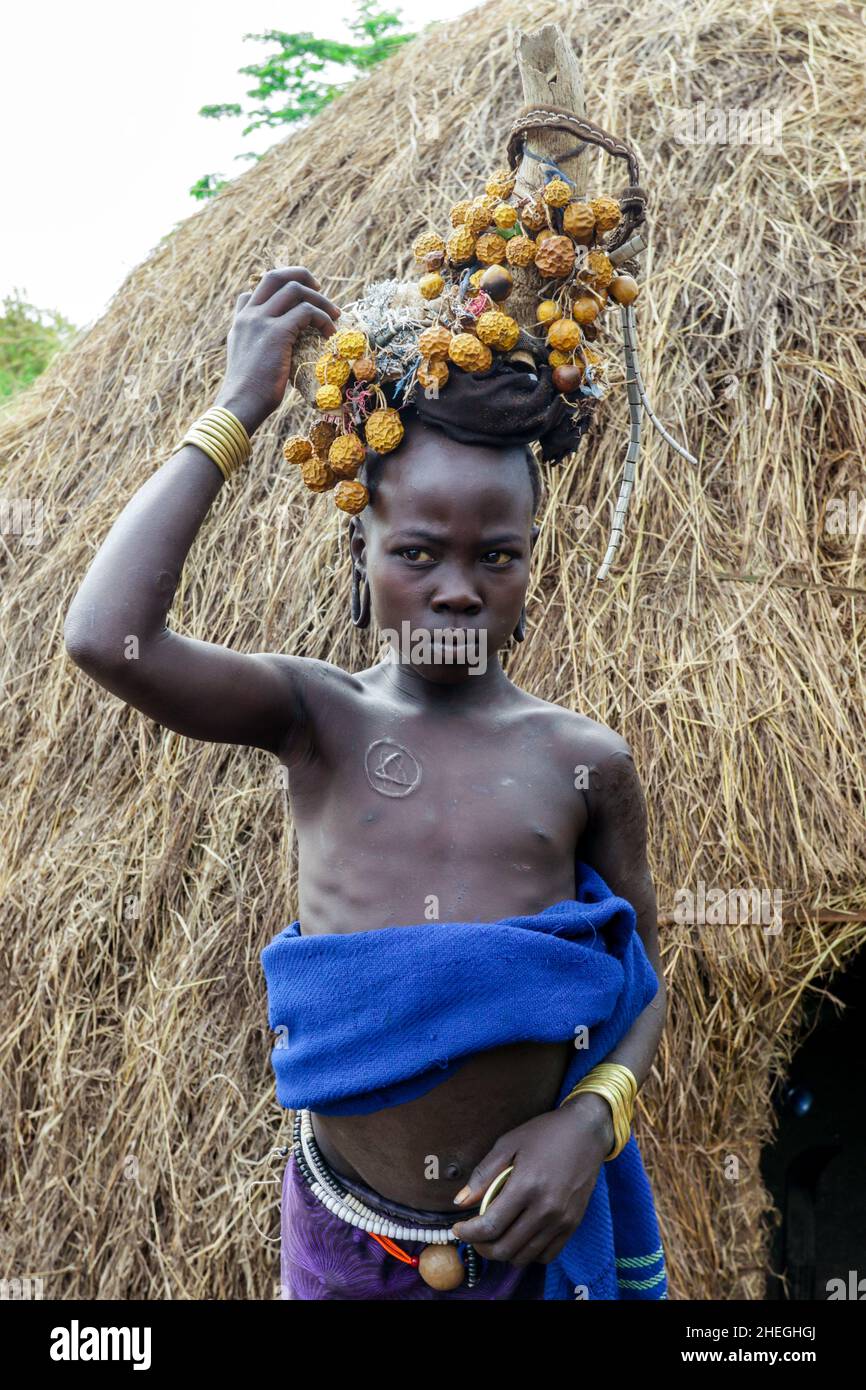 Omo River Valley, Ethiopie - 29 novembre 2020: Portrait d'un adolescent africain avec des boucles d'oreilles traditionnelles en bois et des cornes brisées avec des fleurs jaunes sèches Banque D'Images