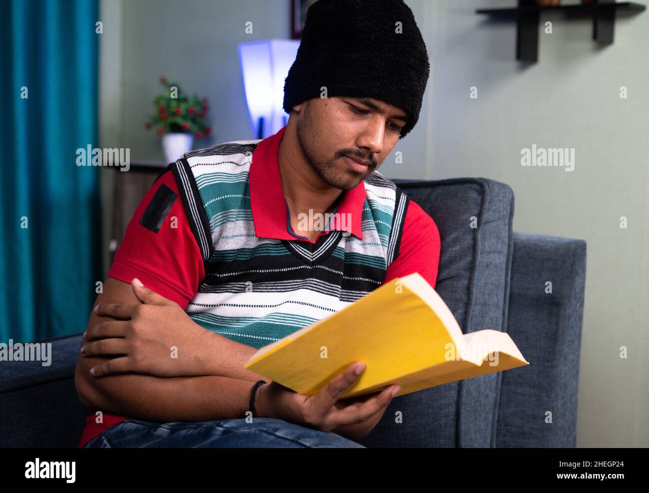 Jeune homme lisant des livres en portant un chandail et une casquette pendant la saison hivernale glaciale à la maison - concept de travail dur et intelligent, étudiant pour l'examen, compétence Banque D'Images