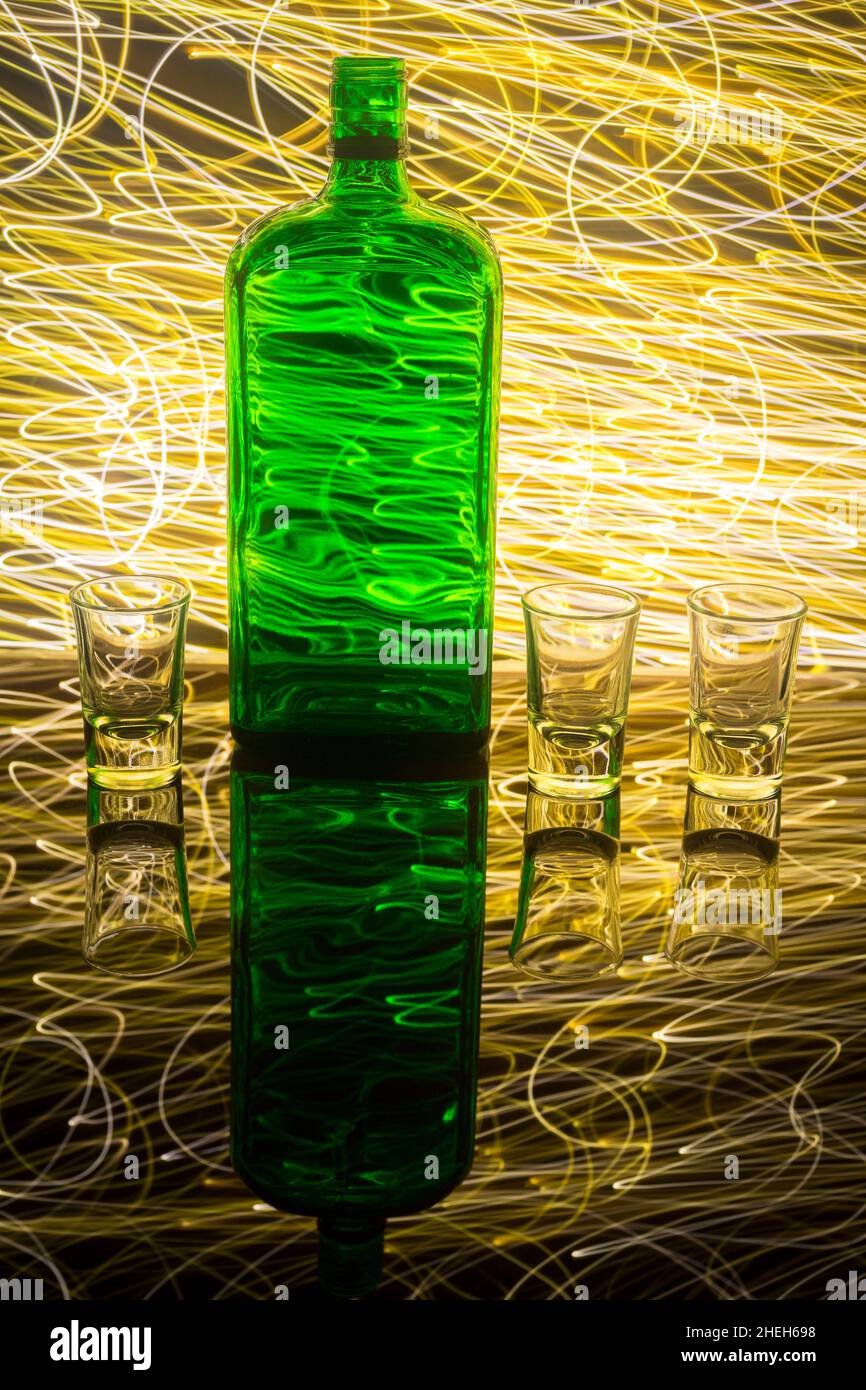 Une bouteille verte avec trois verres à liqueur sur l'arrière-plan qui est illuminée avec une peinture légère. Banque D'Images