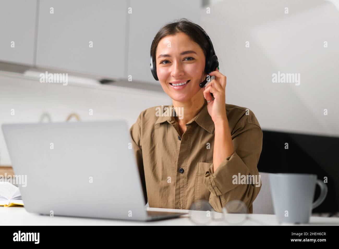 Femme asiatique souriante indépendante portant un micro-casque/oreillette avec un ordinateur portable pour une connexion en ligne avec des collègues ou des clients travaillant à distance, une femme assise dans la publicité du bureau à domicile regarde la caméra Banque D'Images
