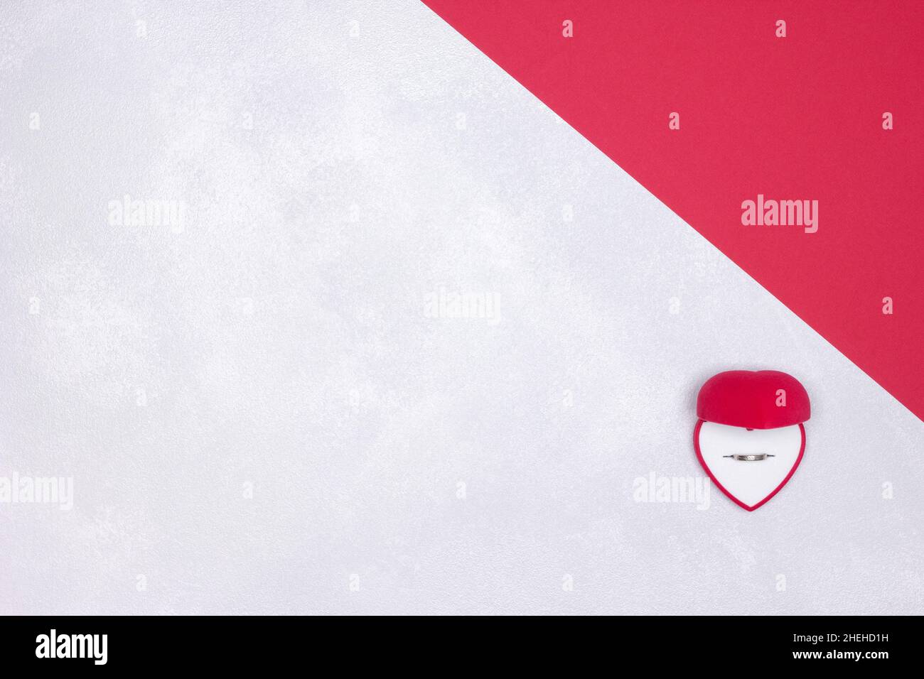 Boîte cadeau ouverte en velours rouge en forme de coeur avec anneau de mariage à l'intérieur sur fond texturé rouge et blanc argenté.Vue de dessus.Copier l'espace Banque D'Images