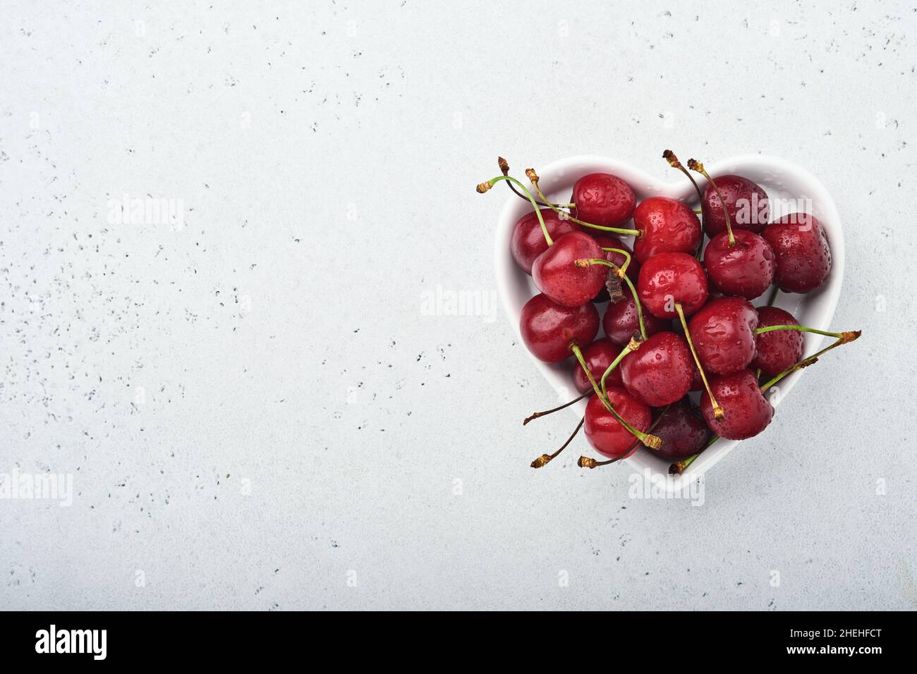 Assiette en forme de cœur blanc à la cerise douce et fraîche pour la Saint-Valentin sur fond gris.Concept pour un repas romantique.Vue de dessus.Maquette. Banque D'Images