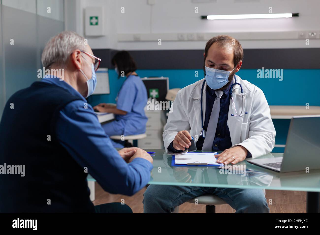 Praticien mettant le sceau médical sur le papier d'ordonnance pour donner la médecine de soins de santé à l'homme âgé en fonction.Médecin utilisant le timbre sur le rapport de visite de contrôle pendant une pandémie de coronavirus. Banque D'Images