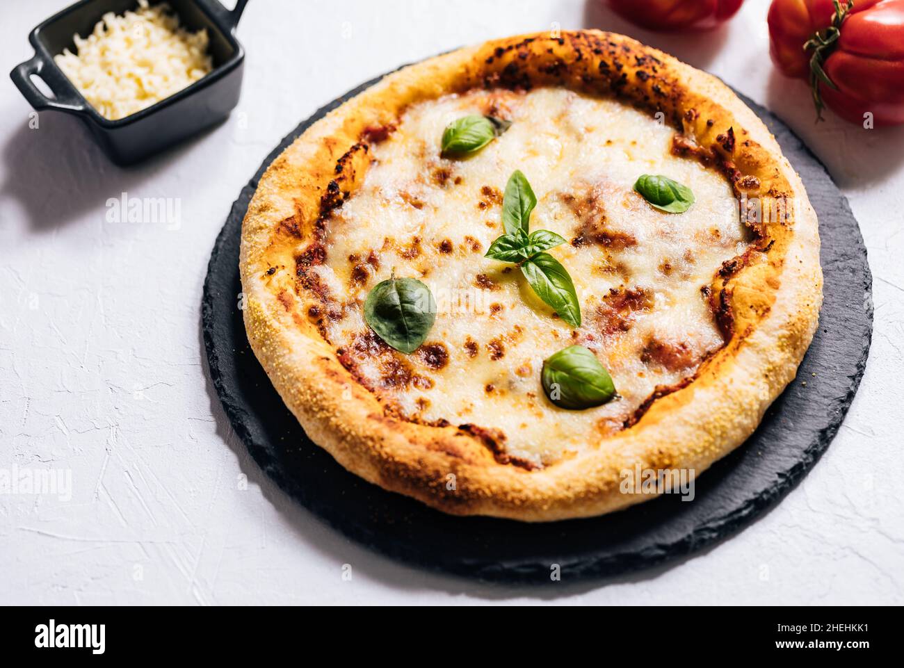 Pizza italienne traditionnelle sur fond rustique blanc avec basilic, tomate, mozzarella, huile d'olive et autres ingrédients. Banque D'Images