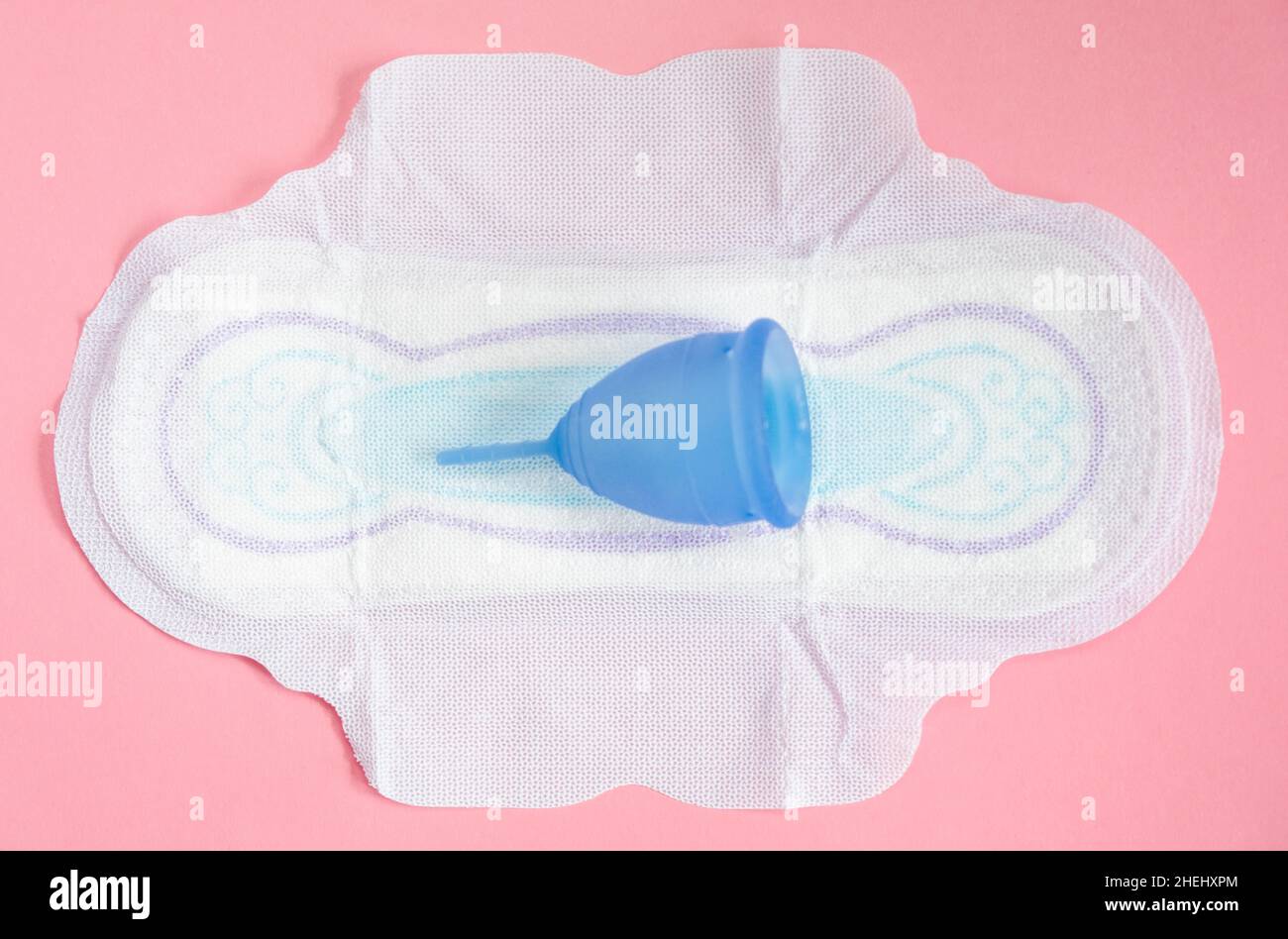 La coupe menstruelle repose sur un coussinet sur fond rose.Concept de choisir un produit écologique qui est sûr pour l'environnement. Banque D'Images