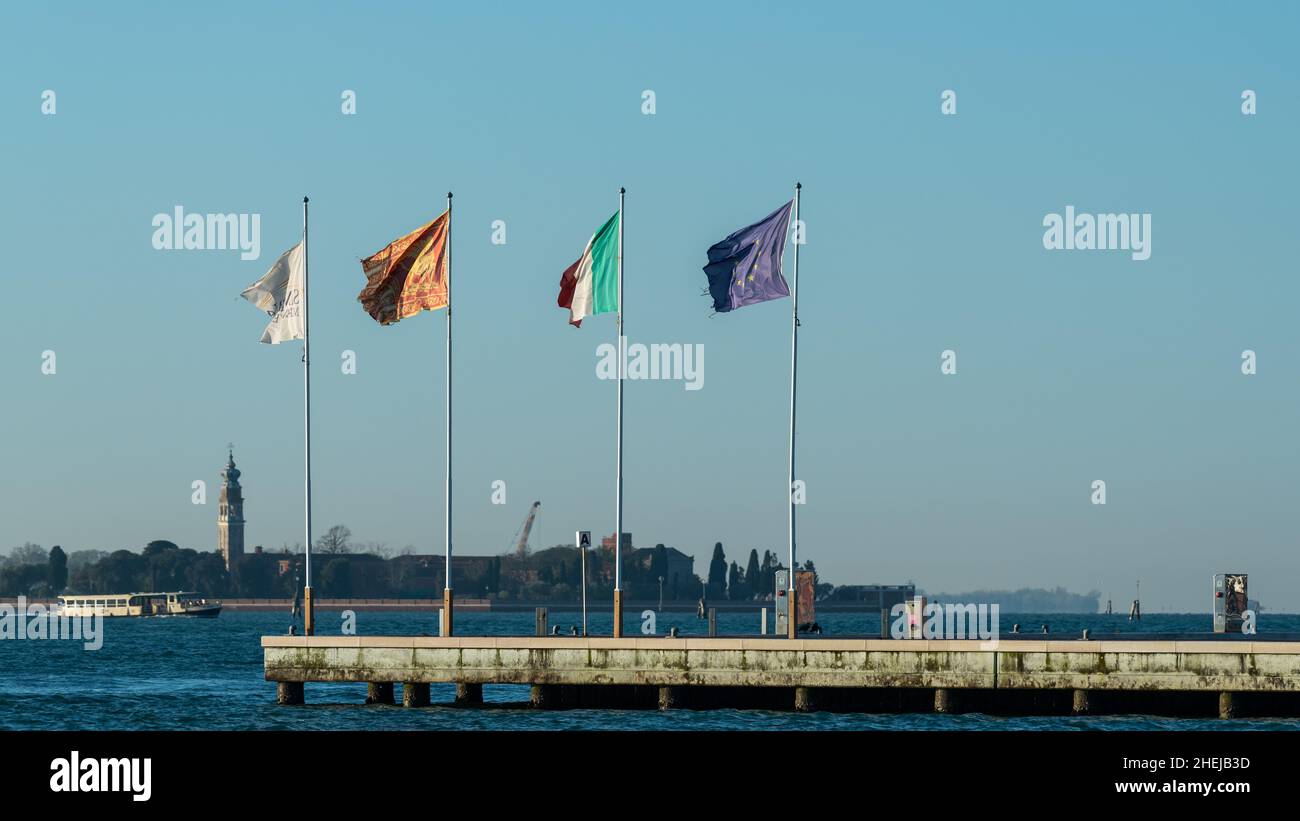Drapeaux sur un quai à Venise (Italie) lors d'une journée ensoleillée et venteuse en hiver Banque D'Images