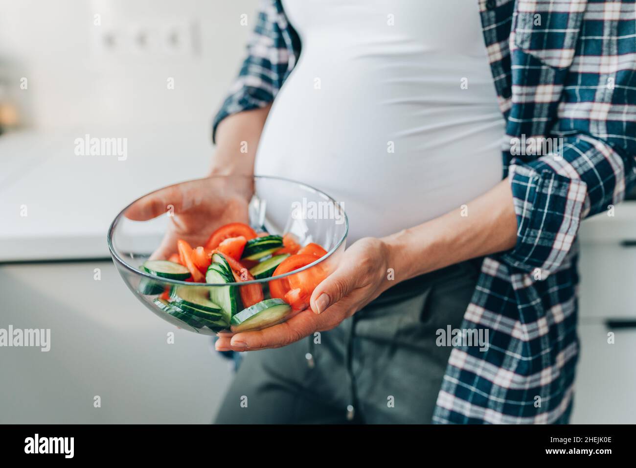 Image rognée femme enceinte tenir un bol avec une salade de légumes de concombres et de tomates dans la cuisine. Banque D'Images