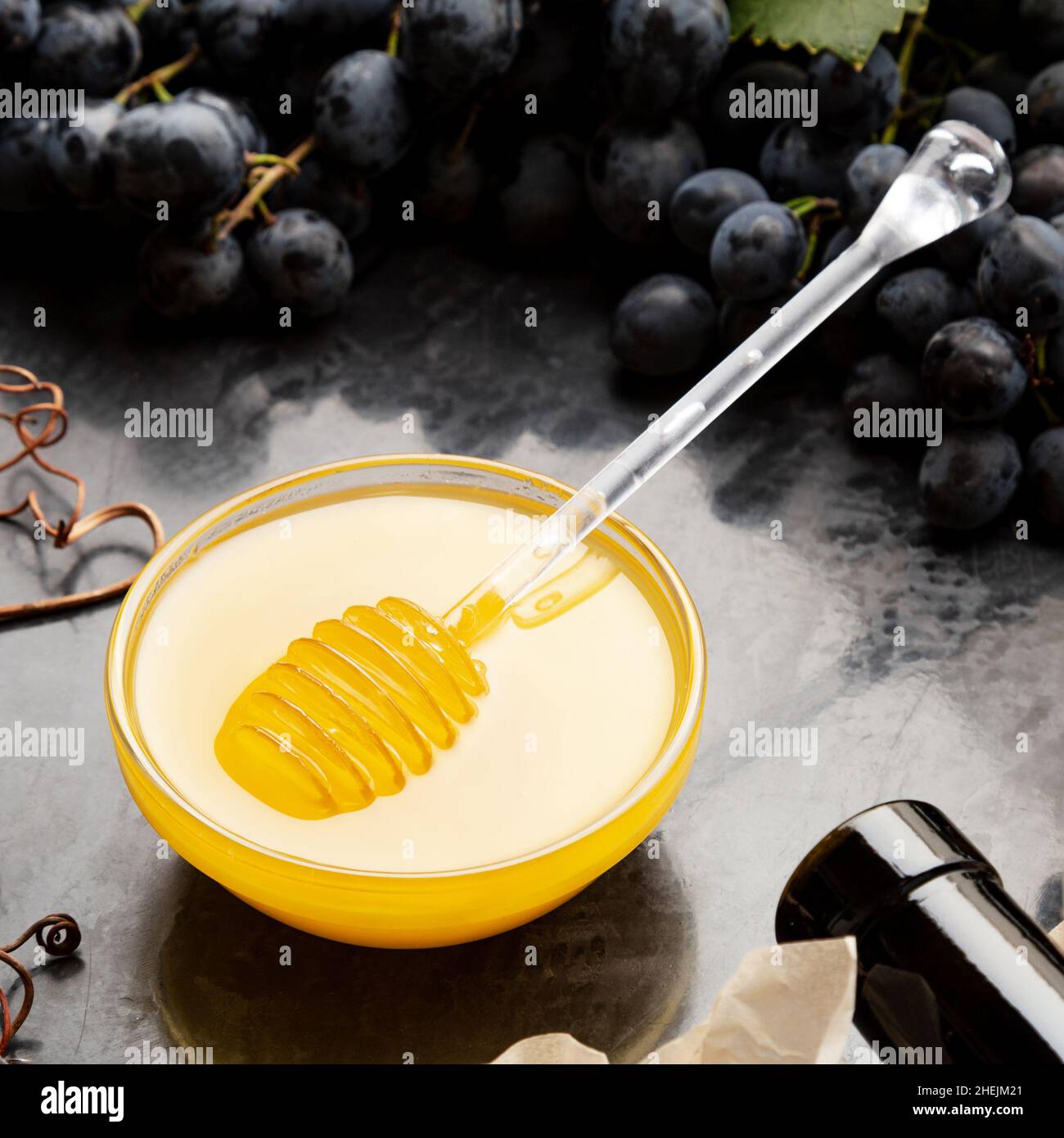 Miel dans un pot en verre avec une cuillère à miel sur une planche en pierre foncée avec un tire-bouchon au fromage à vin dans un cadre de raisin noir juteux. Délicieux miel d'abeille jaune en collation Banque D'Images