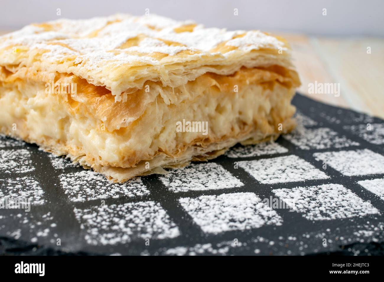 Gros plan d'une crêméschnite ou d'un gâteau à la crème sur une texture en pierre noire avec de la poudre de sucre saupoudrée Banque D'Images