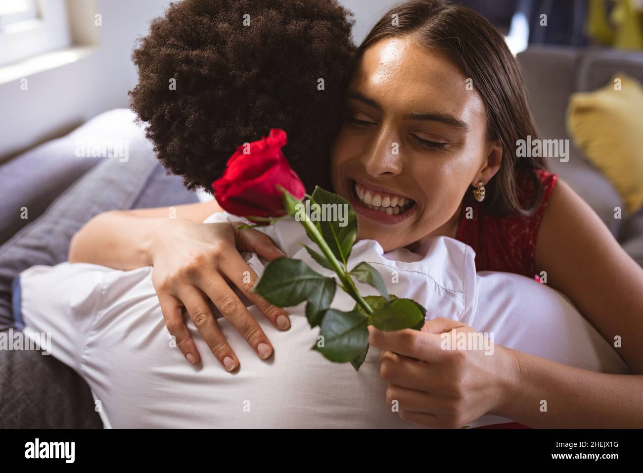 Bonne jeune femme biraciale tenant rouge rose embrassant petit ami à la maison Banque D'Images