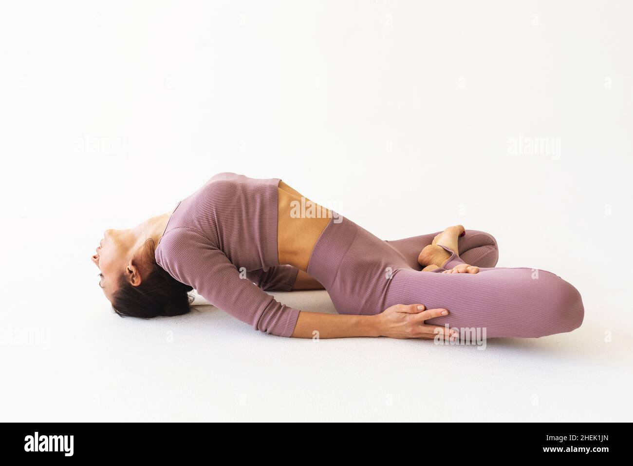 Une femme en sport pratiquant le yoga exécute l'exercice Supta baddha konasana sur un fond blanc Banque D'Images