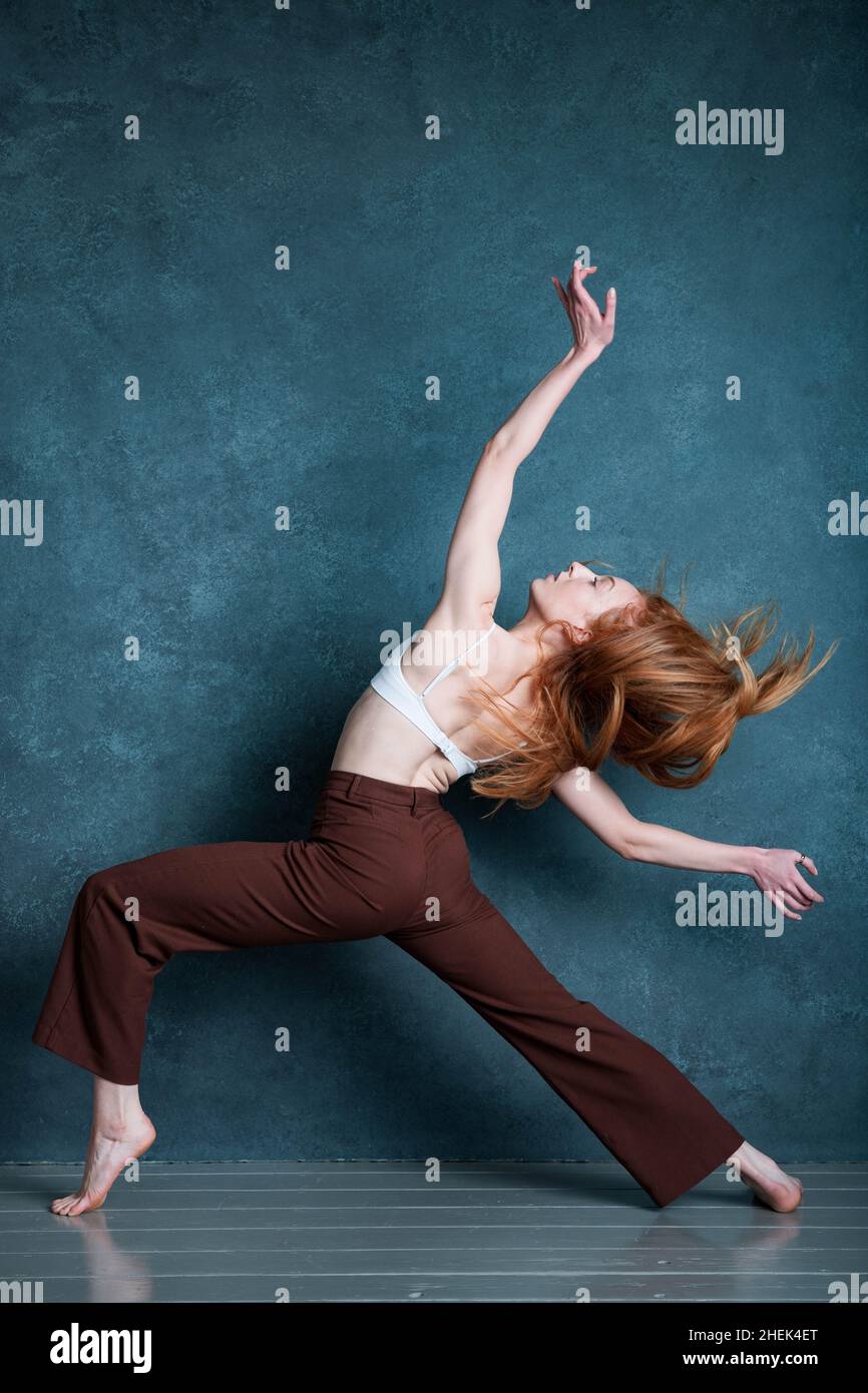 Danseuse Petitie avec des cheveux auburn rouges dansant sur fond gris Banque D'Images
