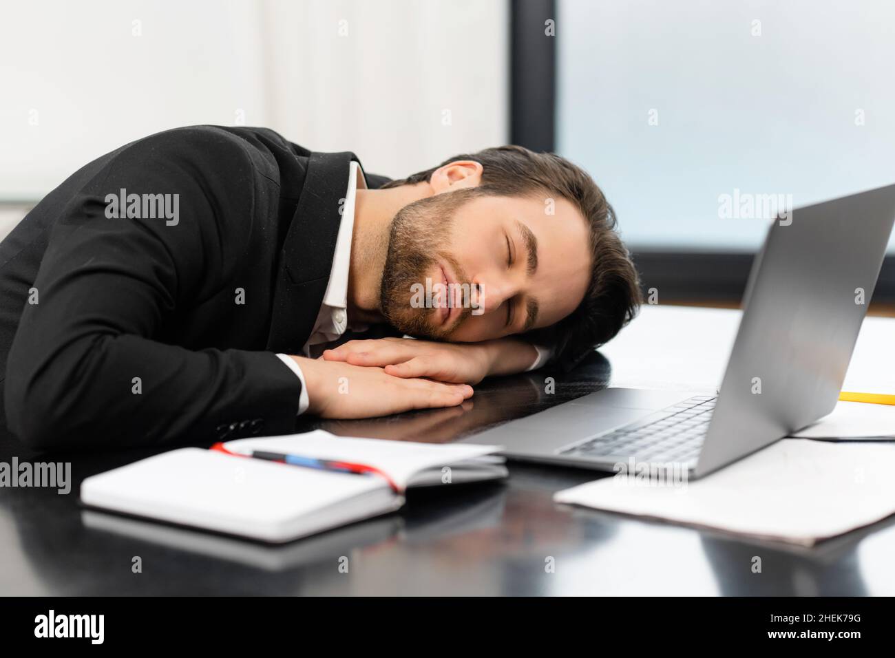 Un jeune homme d'affaires fatigué en tenue officielle fait une sieste sur le lieu de travail, un employé de bureau en costume dormant sur le bureau, prend une pause, travaille trop ou se sent ennuyer Banque D'Images