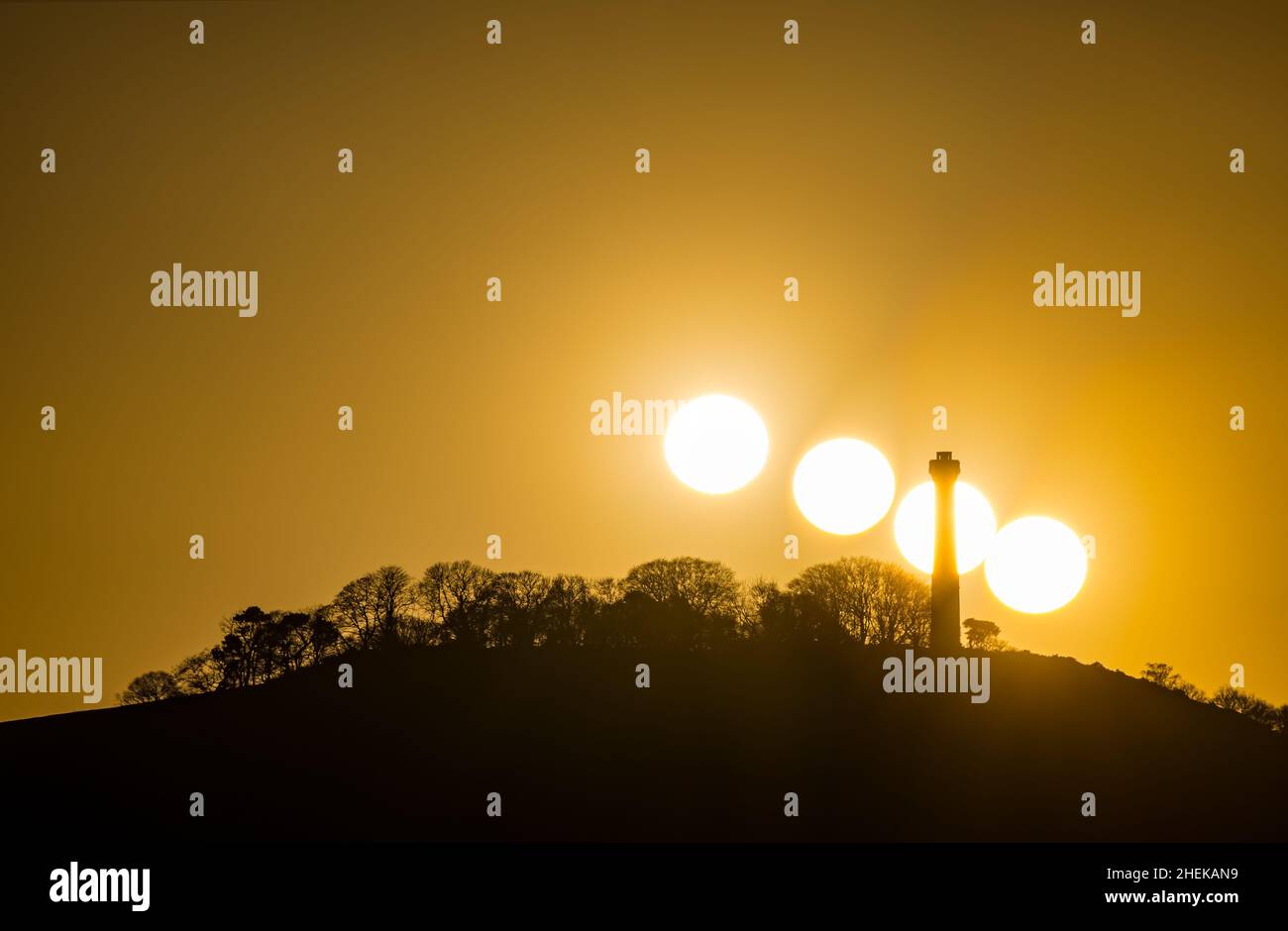 Composite de soleil se coucher dans un ciel orange derrière la silhouette de la tour au sommet d'une colline du Hopetoun Monument, East Lothian, Écosse, Royaume-Uni Banque D'Images