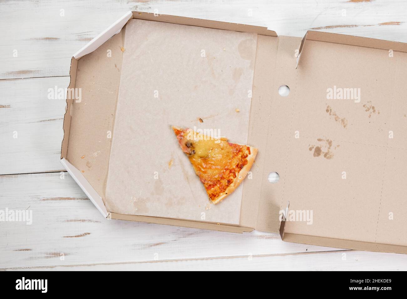 Un dernier morceau de pizza dans une boîte en carton. Fond en bois blanc.Concept alimentaire.Vue de dessus. Banque D'Images