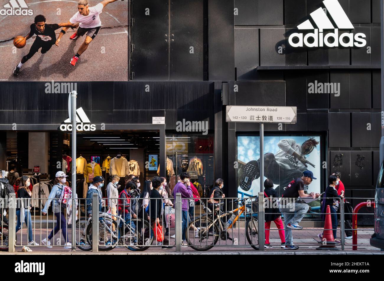 Des piétons marchent devant la marque allemande multinationale de vêtements de sport Adidas magasin et logo à Hong Kong. Banque D'Images