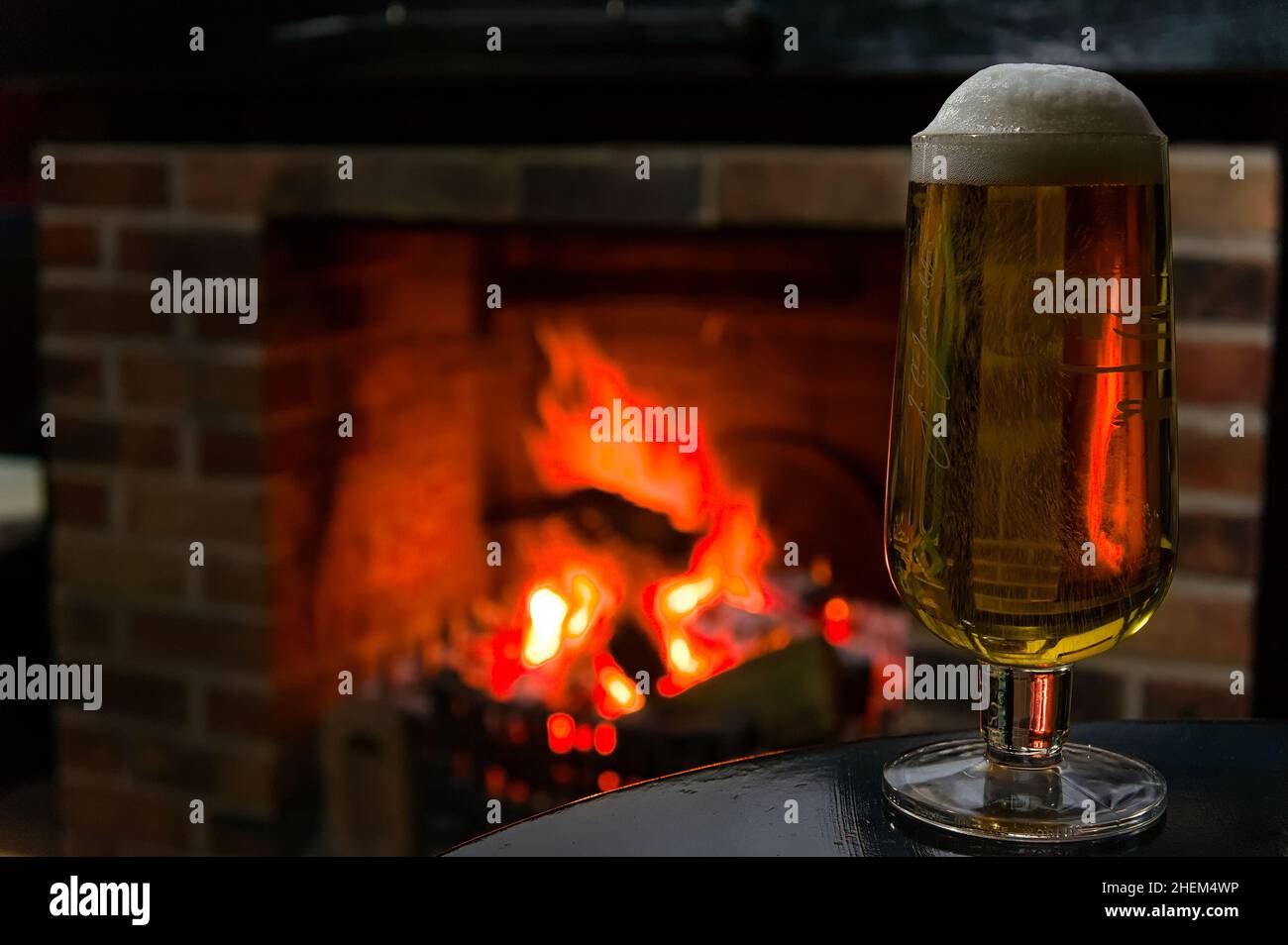 Une pinte complète de bière sur une table avec une cheminée brûlante défocalisée en arrière-plan. Banque D'Images