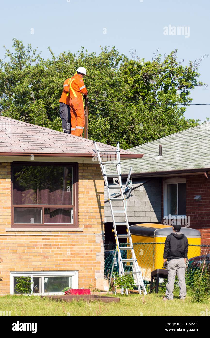 Toronto, Canada, 2015: Les travailleurs qui fixent des fils électriques à un poteau au-dessus d'une maison. Banque D'Images