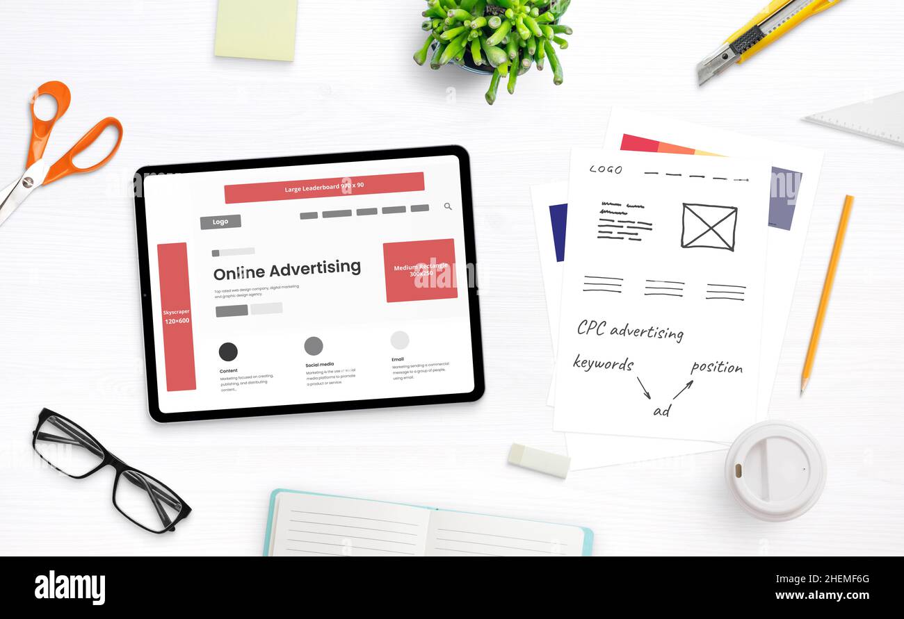 Planification d'un concept de campagne publicitaire en ligne.Tablette avec page Web et positions publicitaires entourées de fournitures de bureau et de notes Banque D'Images