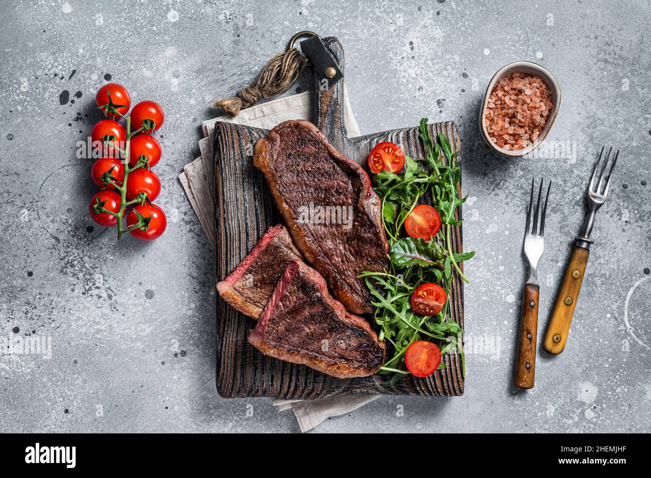 Steak de viande de bœuf rôti au chapeau ou au sirloin supérieur sur une planche de bois avec salade.Arrière-plan gris.Vue de dessus Banque D'Images