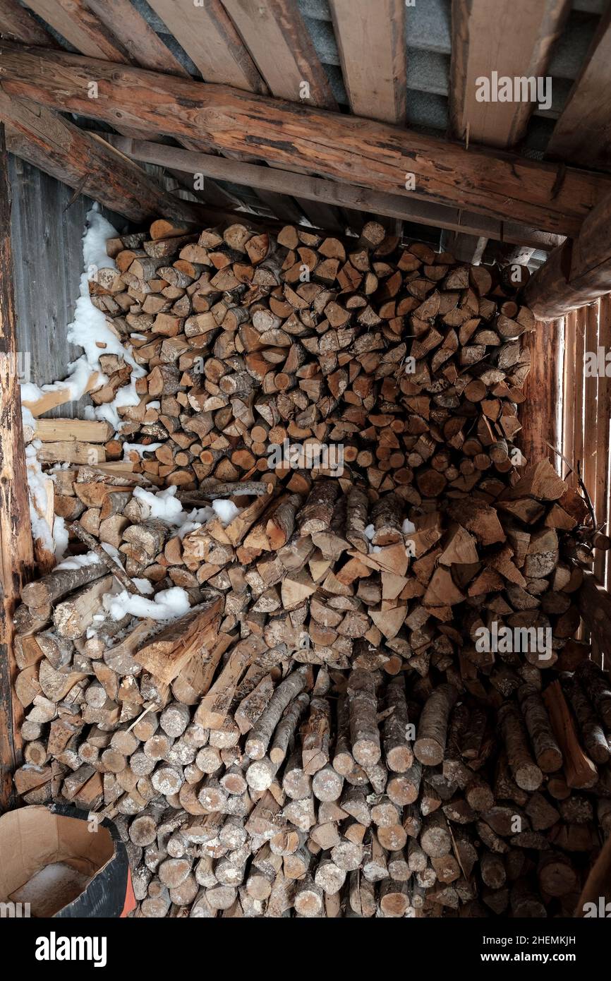 Bois de chauffage empilé dans une ancienne grange, partiellement couvert de neige à travers les murs de la planche.Saison de chauffage dans le village.Style de vie rustique. Banque D'Images