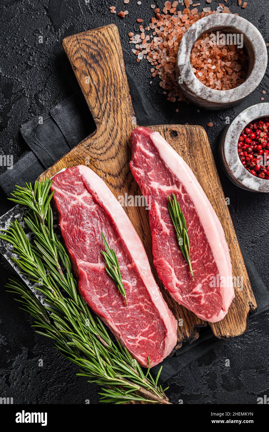 Steak de viande de bœuf de boucherie ou sirloin sur le dessus du butcher.Arrière-plan noir.Vue de dessus Banque D'Images