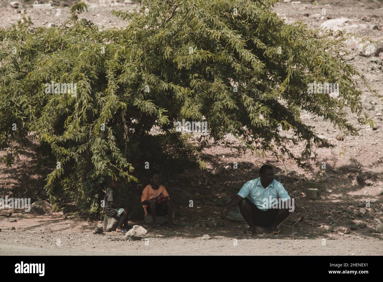 Djibouti, Djibouti - 21 mai 2021 : un homme djiboutien et ses deux fils assis sur la pierre et attendant le bus sous l'ombre d'un arbre à Djibouti.Editeur Banque D'Images