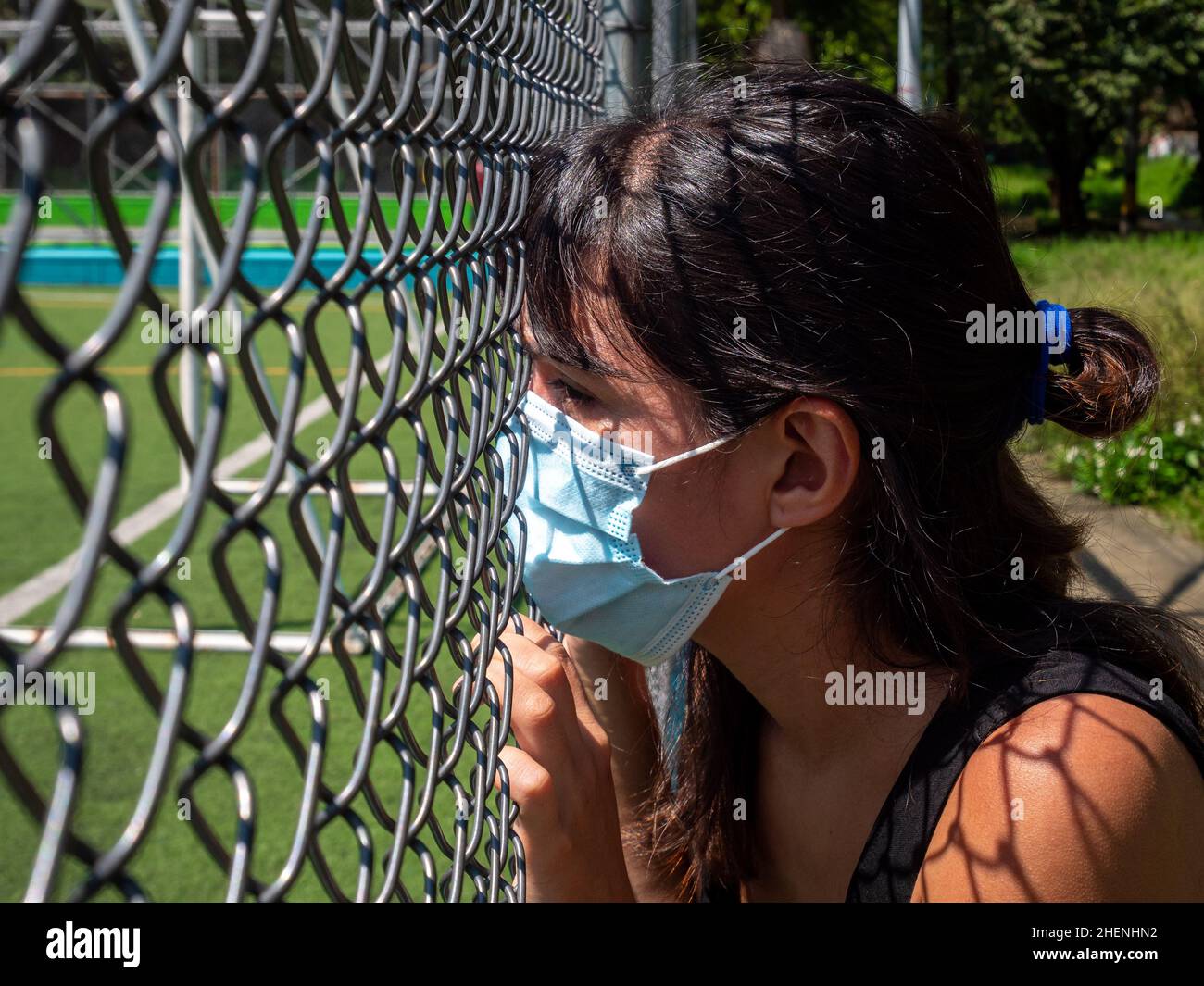 La jeune femme Brunette qui utilise un masque bleu regarde à travers le maillage du terrain de football Banque D'Images