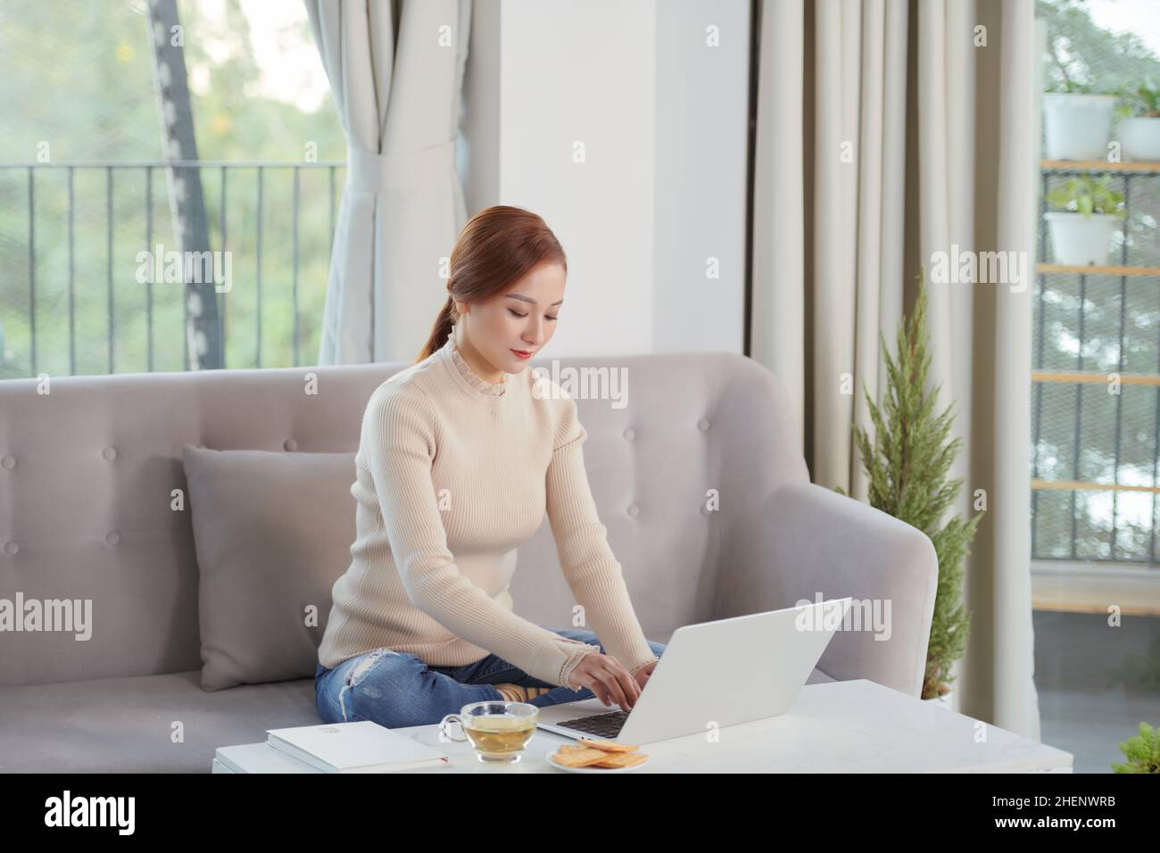 belle femme s'asseoir sur le canapé et utiliser l'ordinateur portable et la connexion pour le travail Banque D'Images