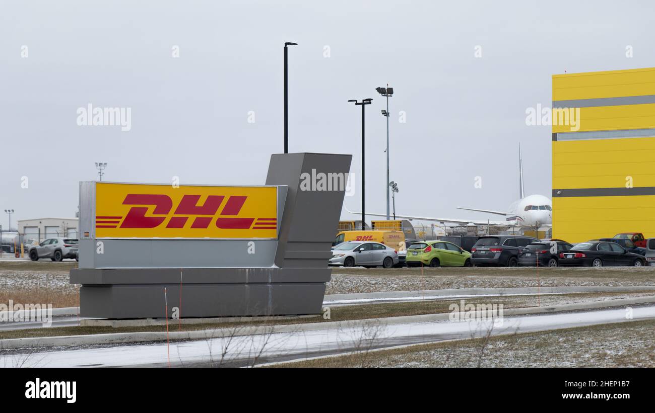 Un panneau DHL se trouve devant une nouvelle installation de fret à l'aéroport de Hamilton ; un avion de fret est vu en arrière-plan. Banque D'Images