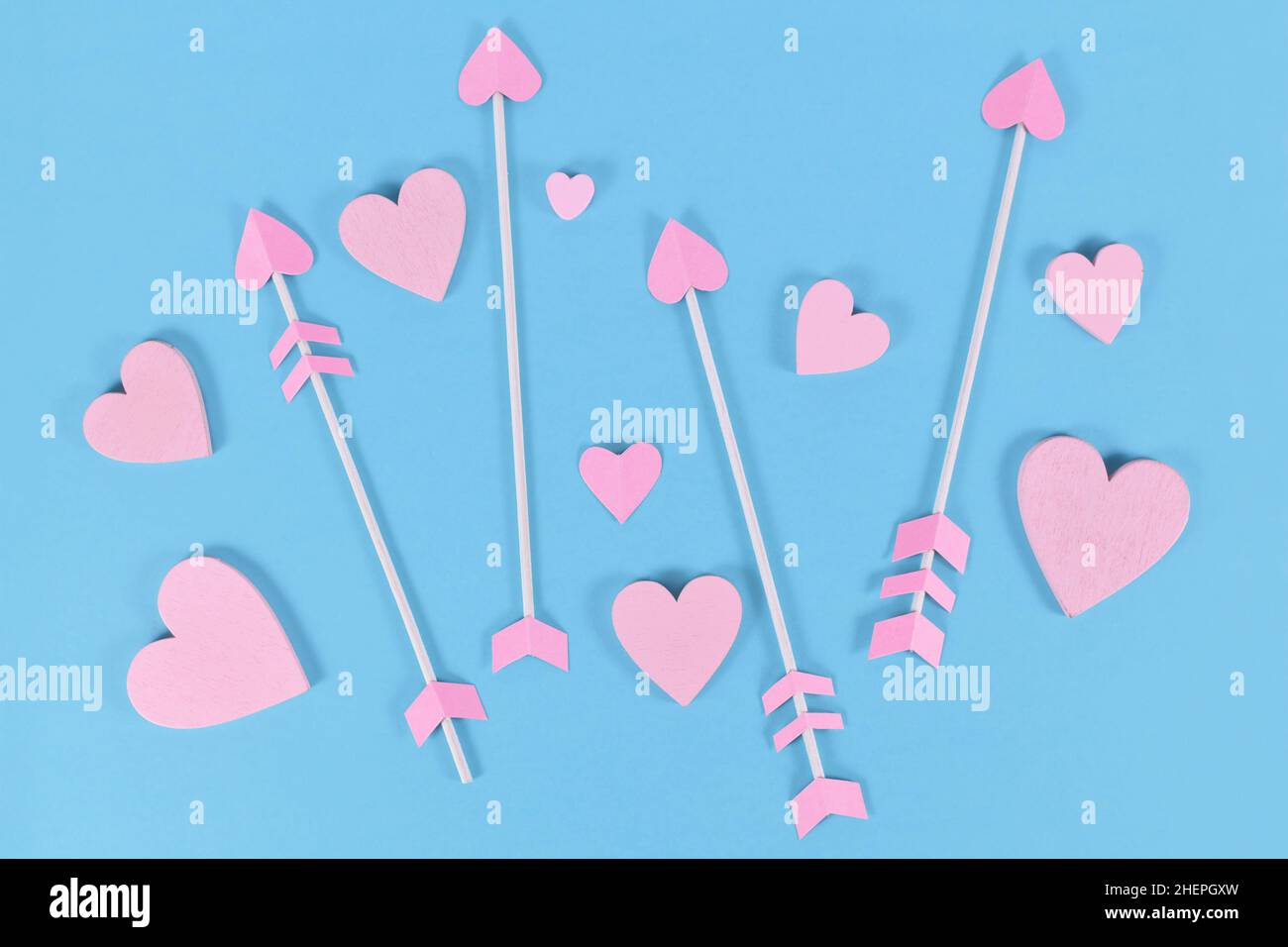 Rose Saint-Valentin flèches de cupidon avec bouts en forme de coeur et ornements de coeur sur fond bleu Banque D'Images