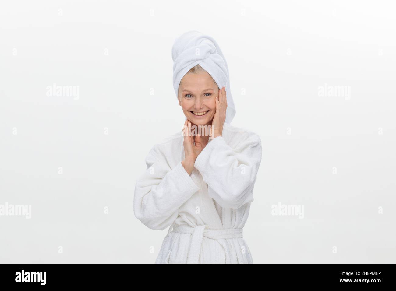 femme adulte féminine plus âgée portant un peignoir et une serviette au-dessus de sa tête souriante isolée sur fond blanc Banque D'Images