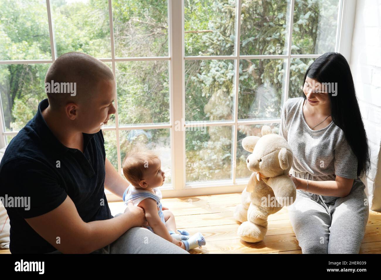 Jeune couple avec un bébé jouant et assis sur le seuil de la fenêtre dans une nouvelle maison Banque D'Images