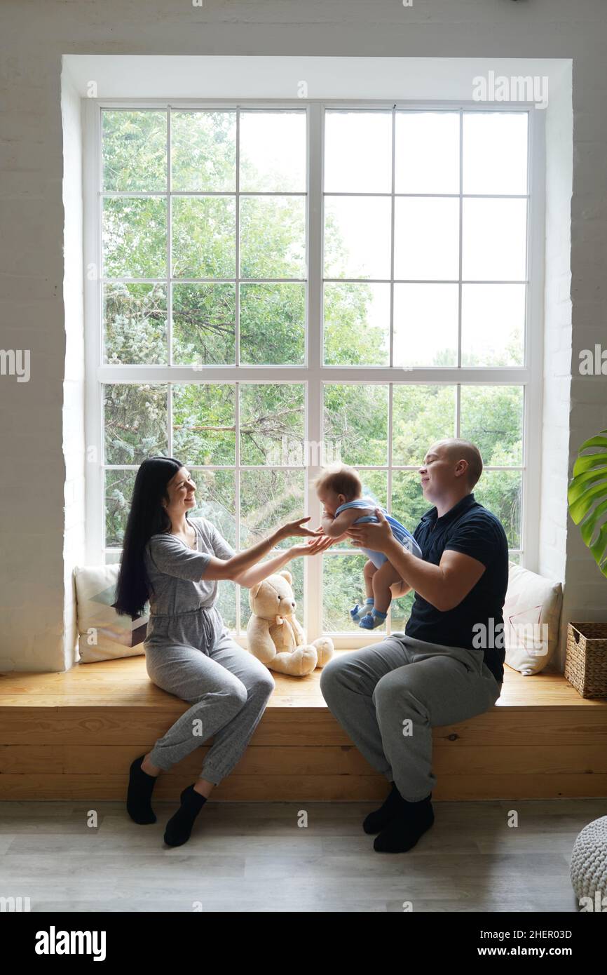 Jeune couple avec un bébé jouant et assis sur le seuil de la fenêtre dans une nouvelle maison Banque D'Images