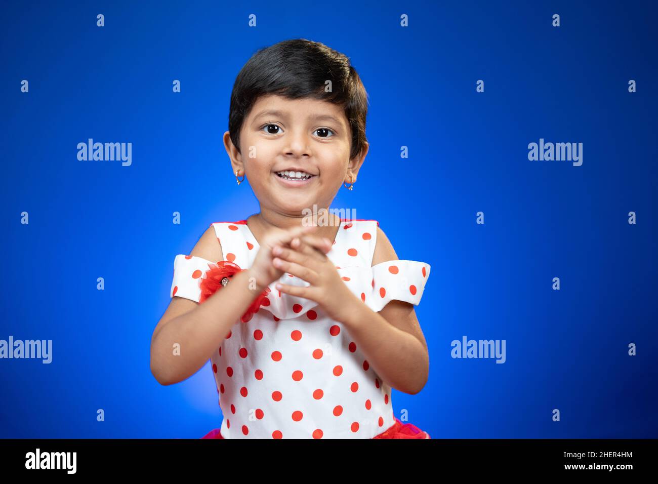 Indienne bonne petite fille applaudissant les mains sur fond bleu en regardant la caméra - concept de style de vie ludique d'enfance, applaudissant et en appréciant. Banque D'Images