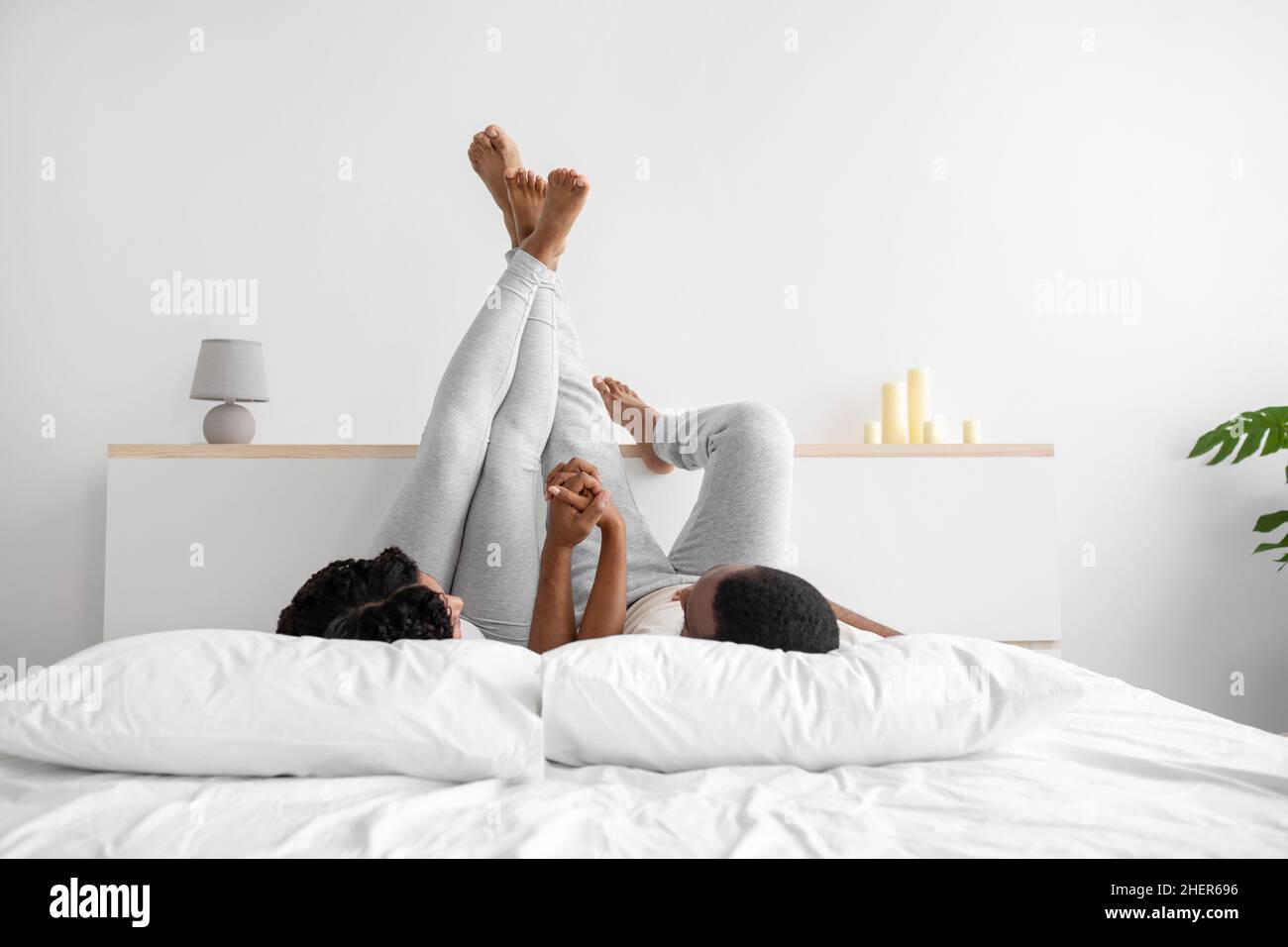 Jeune femme noire aimante et homme ont levé leurs jambes, tenez les mains,  allongez-vous sur le lit blanc confortable, reposez-vous ensemble Photo  Stock - Alamy