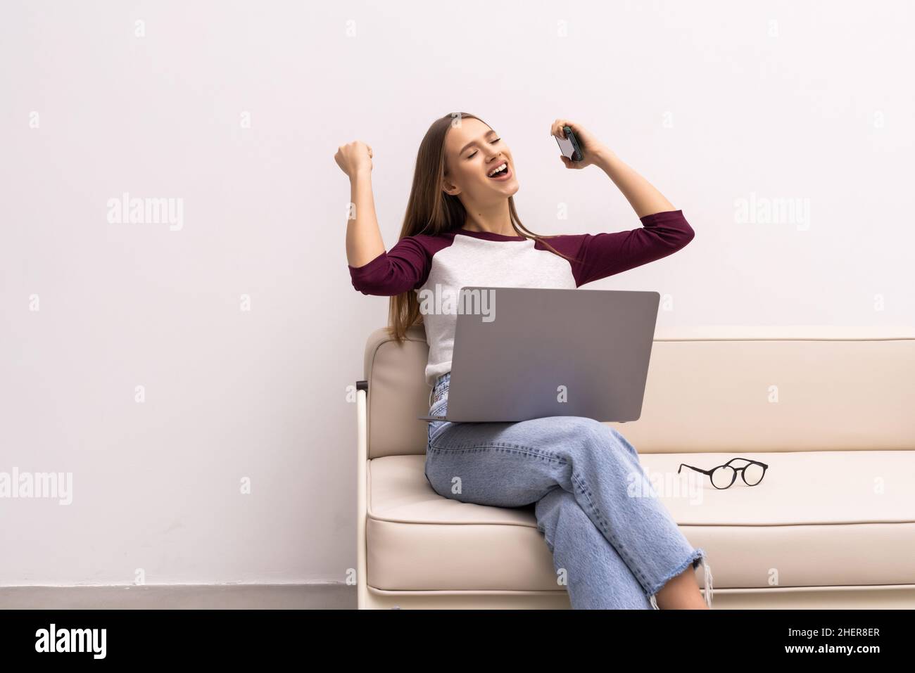 Portrait d'une femme assise sur le sol et regardant l'écran de l'ordinateur portable, tenant le téléphone et la carte, le compte de la banque, la loterie gagnante, créditant une grande AMO Banque D'Images