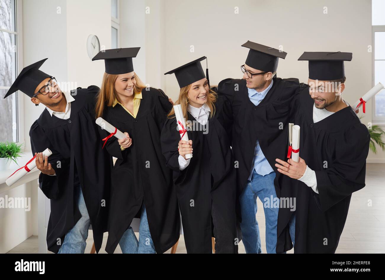 Divers groupes d'amis heureux de l'université qui s'embrasent dans la salle de classe après la cérémonie de remise des diplômes Banque D'Images