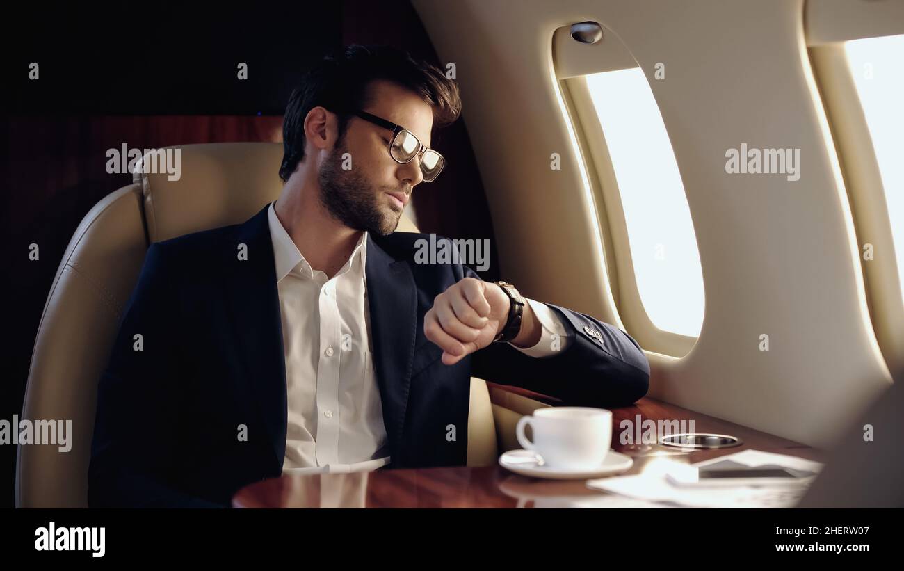 Homme d'affaires regardant une montre-bracelet près d'un café et d'un téléphone portable dans un avion privé Banque D'Images