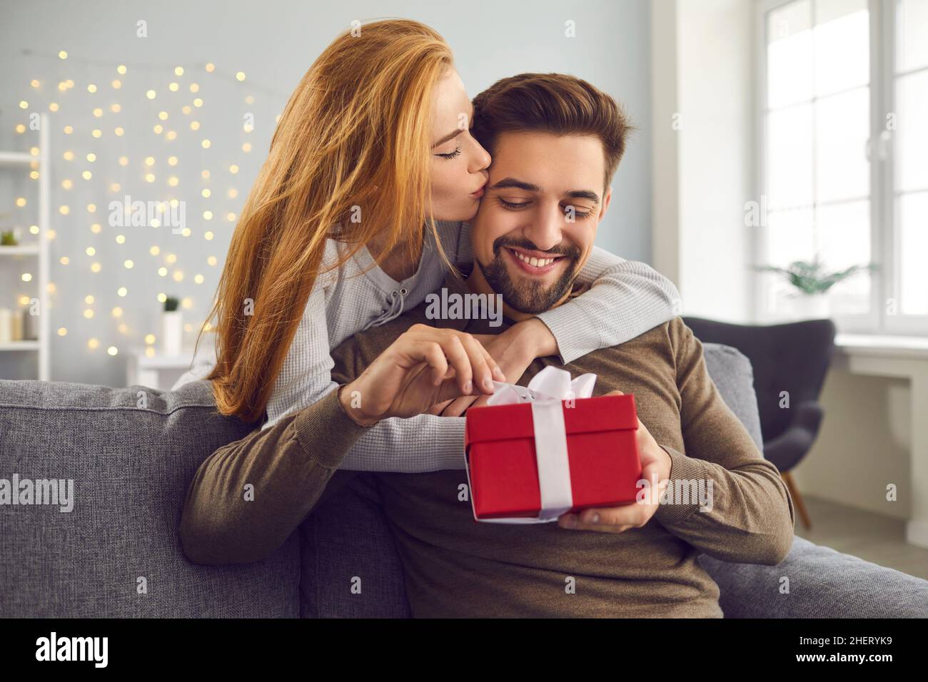 Une jeune femme à tête rouge enserre et embrasse son mari sur la joue lui donnant un cadeau pour la Saint-Valentin. Banque D'Images