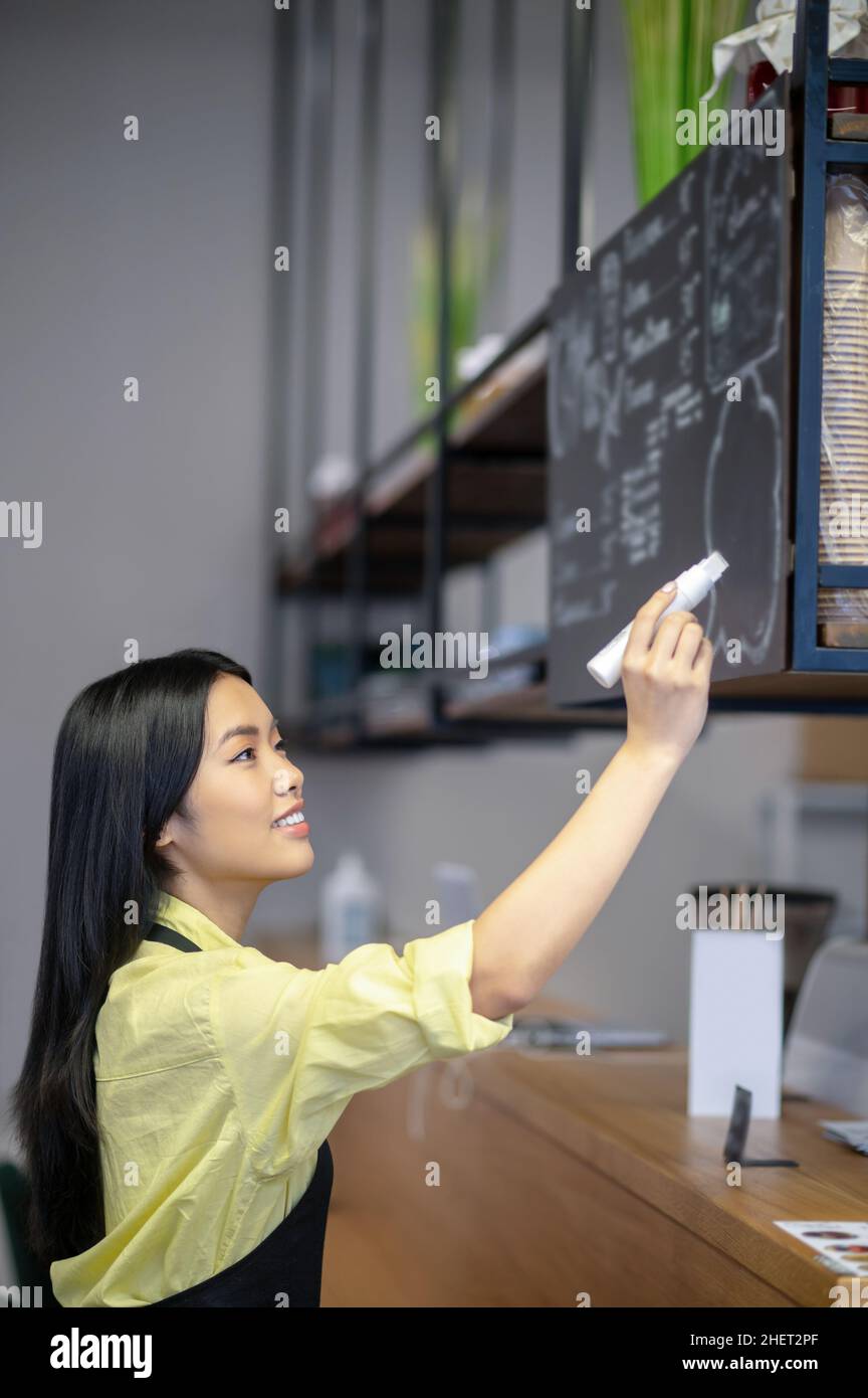 Une jeune femme asiatique écrit un menu à bord dans un café Banque D'Images