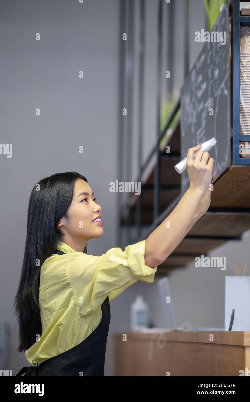 Une jeune femme asiatique écrit un menu à bord dans un café Banque D'Images