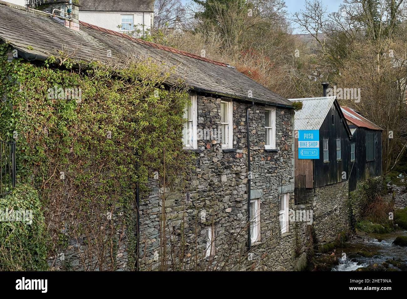 Panneau bleu de la boutique de vélos sur un ancien bâtiment en bois surplombant un ruisseau à Ambleside, Cumbria, Royaume-Uni Banque D'Images