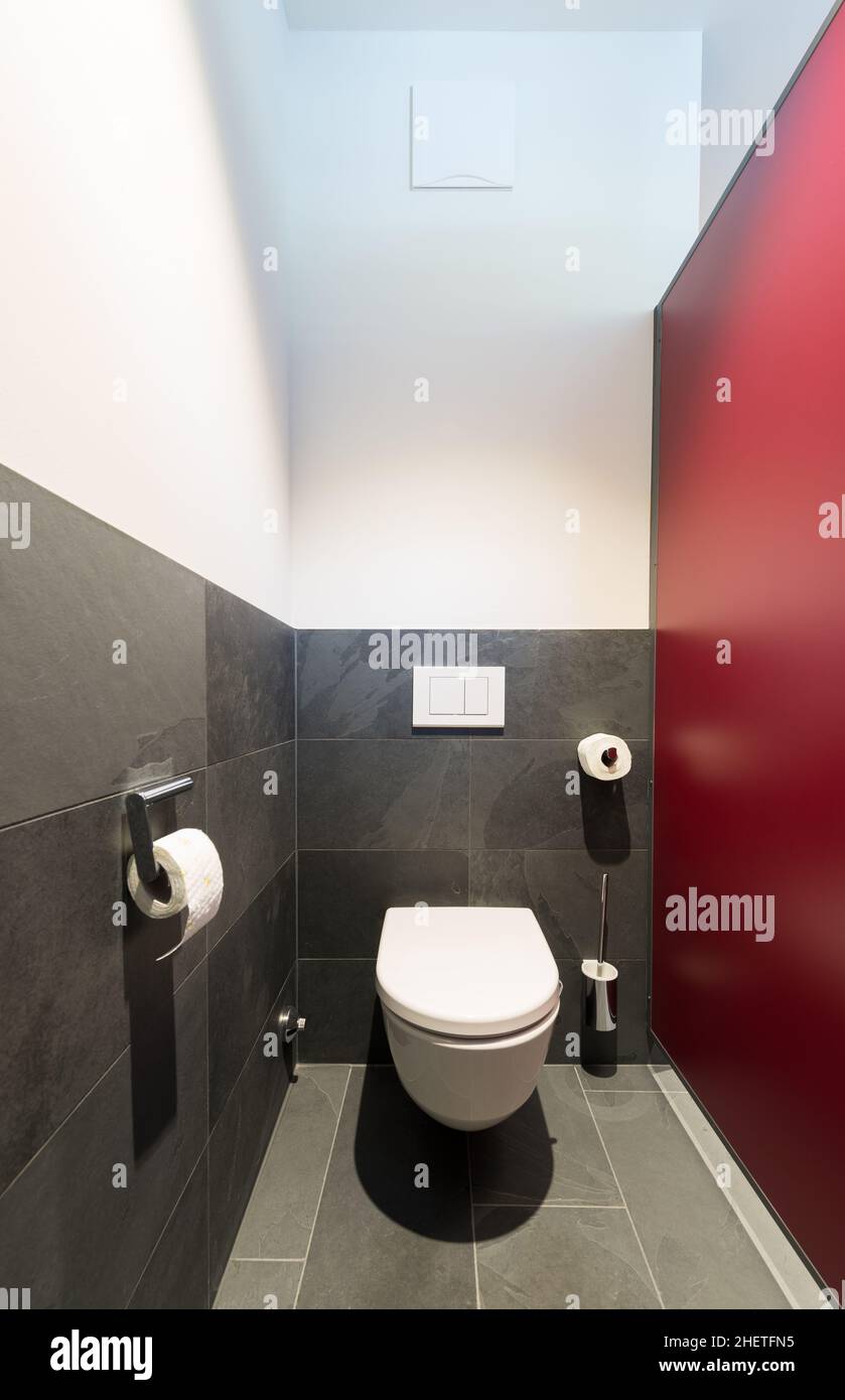 cuvette de toilette moderne avec carreaux gris foncé en ardoise et mur de division rouge Banque D'Images