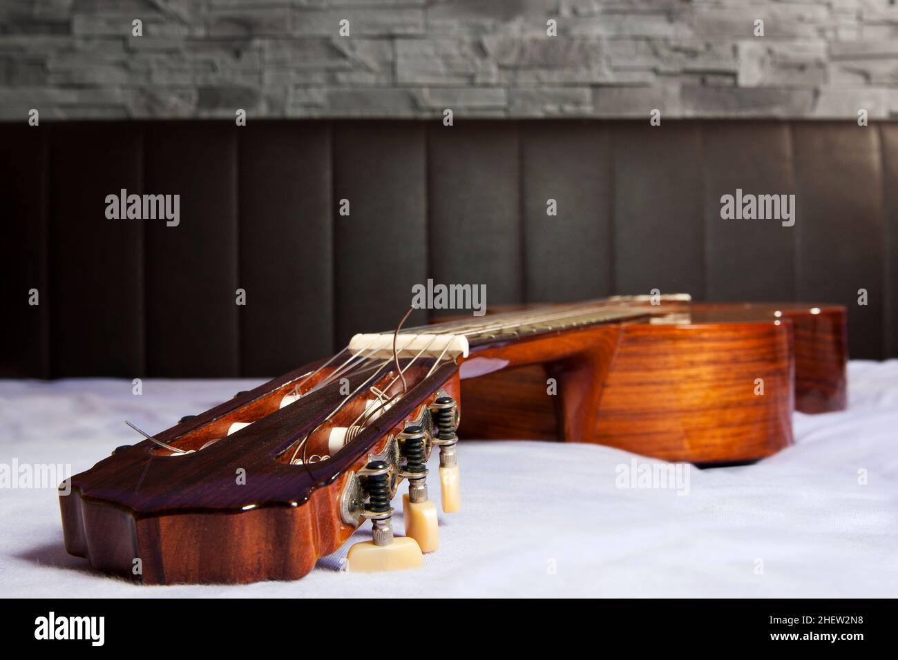 guitare classique couchée sur le lit devant un dos en cuir marron et un mur  en pierre Photo Stock - Alamy